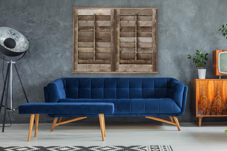 A jewel-toned sofa adds a pop of color to an otherwise neutral-colored room. A blue couch against a gray wall with reclaimed wood interior shutters