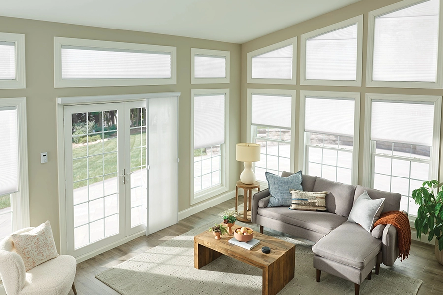 Use custom matching window treatments on windows of different shapes and sizes to help a space feel cohesive. White sheer shades on living room windows of different sizes and shapes