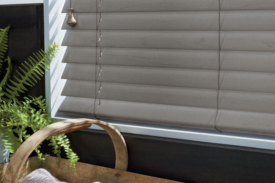 Custom wood and faux wood blinds fit your windows perfectly for smooth operation.  A close up view of gray blinds in a window